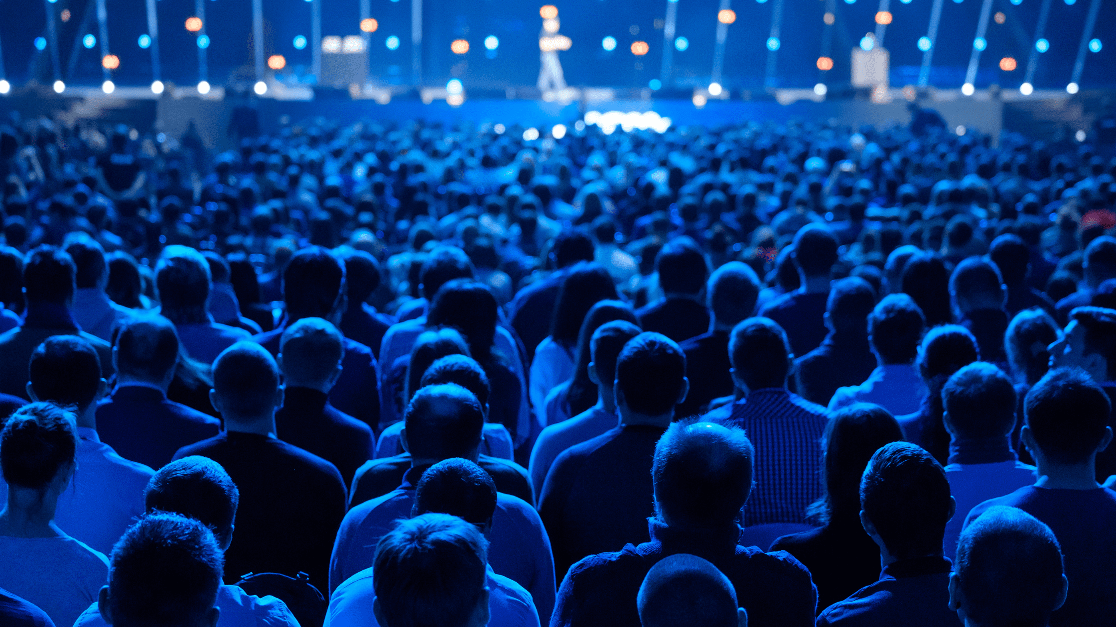 A large audience gathered in front of a stage, illuminated by vibrant blue lighting