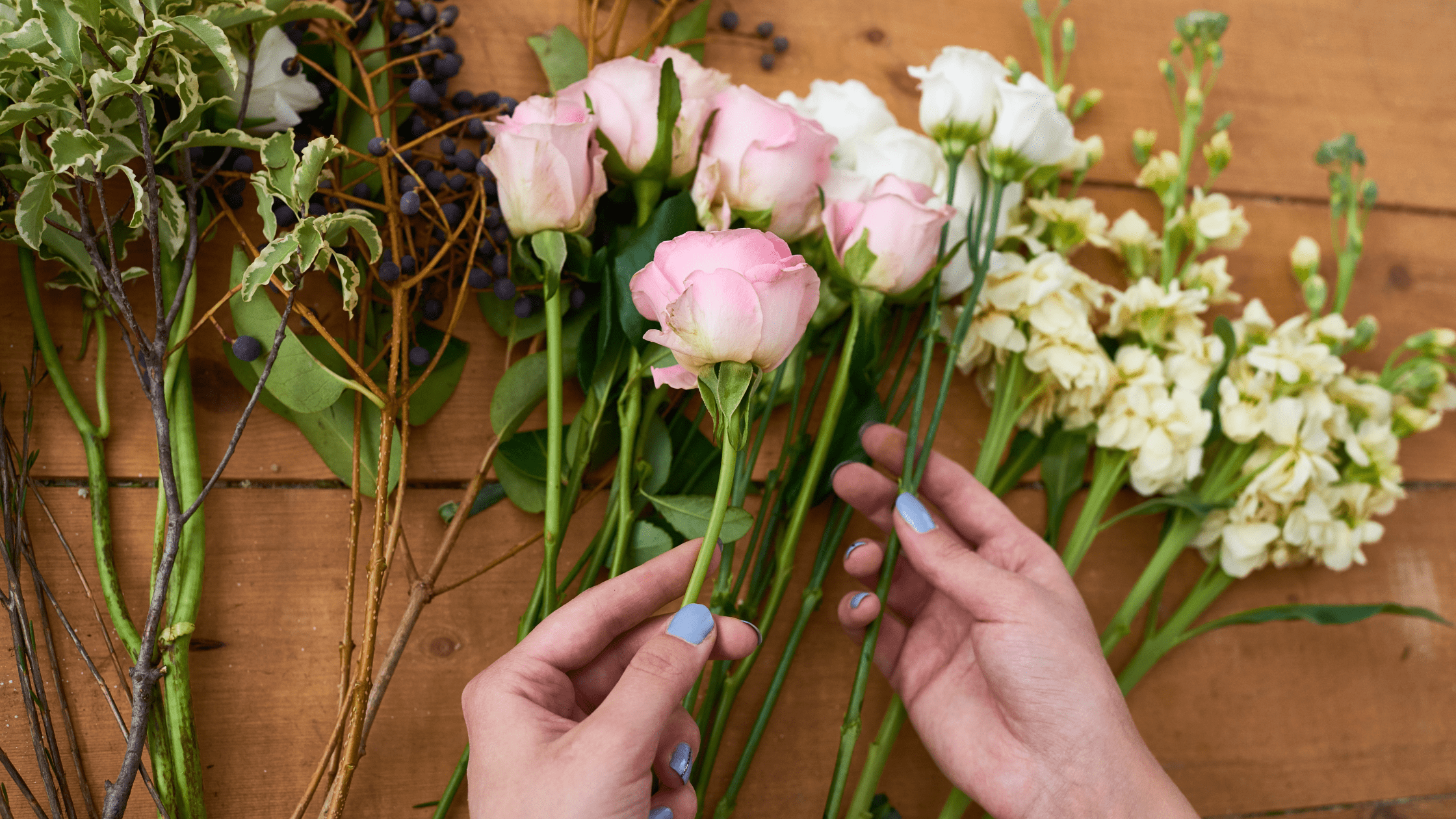 Hands with blue-painted nails carefully arranging fresh flowers for event decor, creating a beautiful floral display.