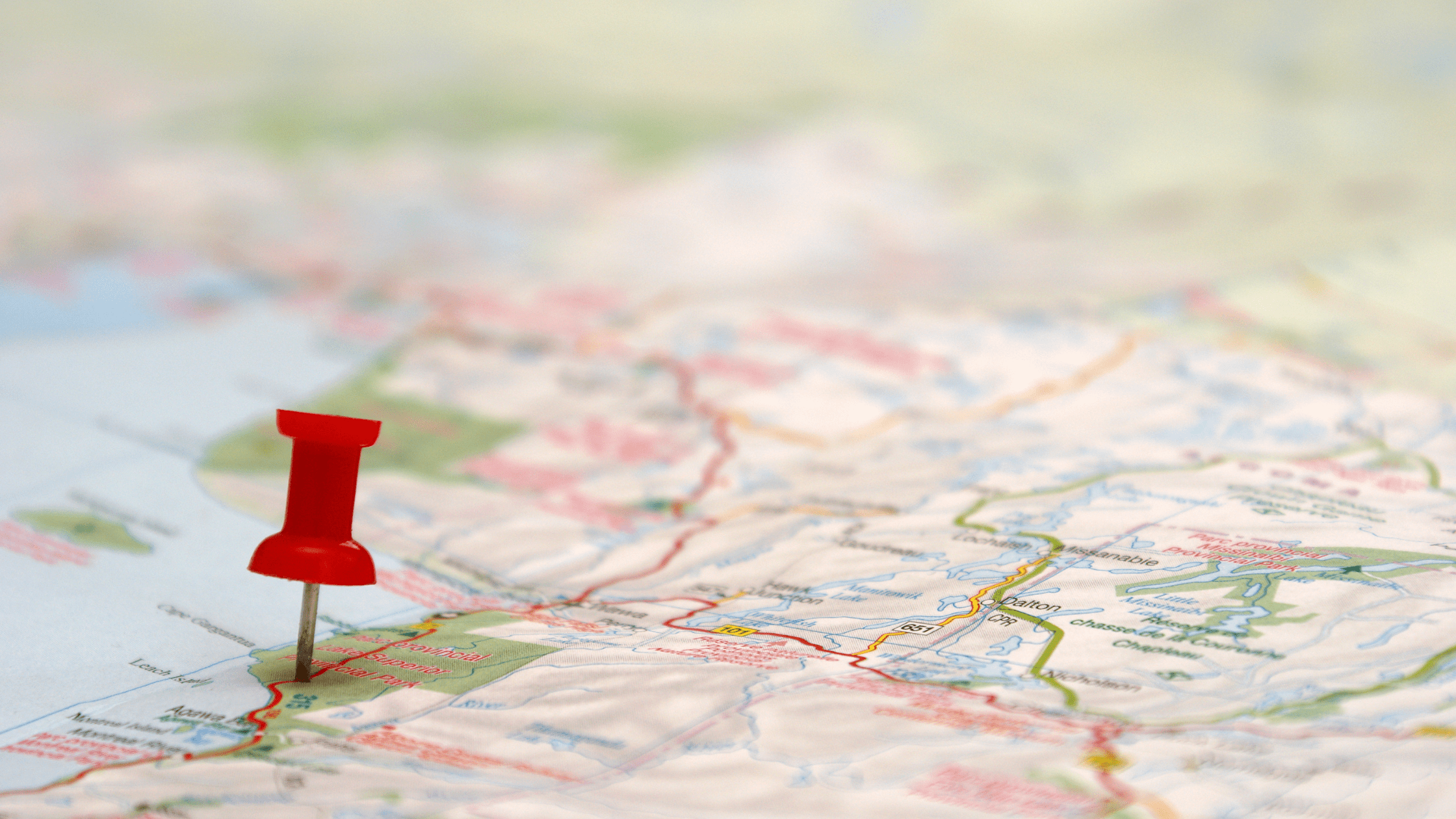 A blurred map with a red push pin marking a destination, symbolizing event planning and logistics