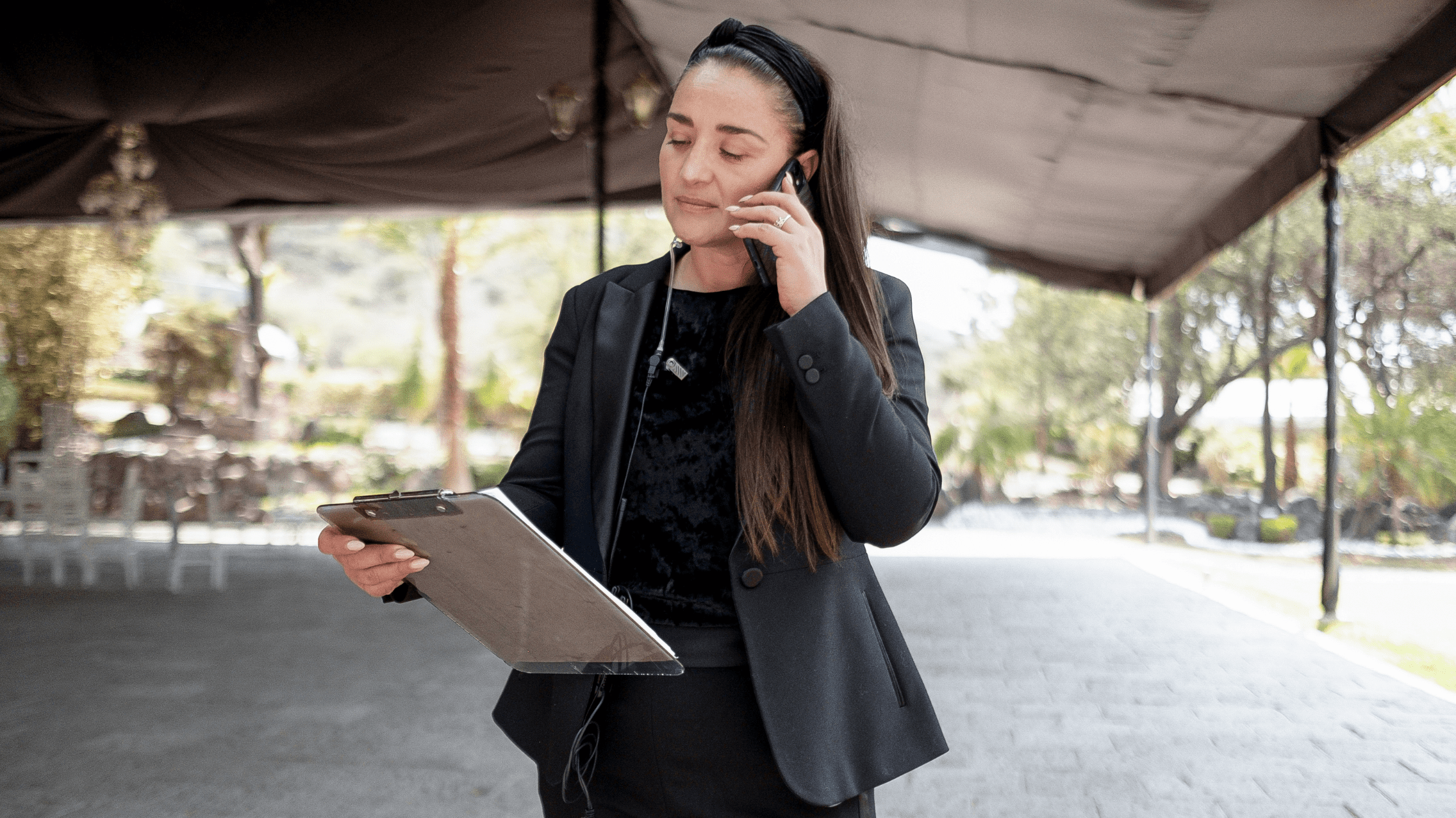 An event planner onsite, speaking on the phone while holding a clipboard, managing event logistics.